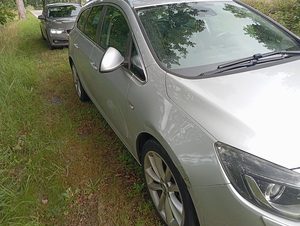 na poboczu stoi srebrny Opel Astra z wygiętym prawym lusterkiem. Za nim stoi nieoznakowany policyjny radiowóz