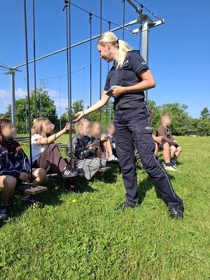 policjantka wręcza ulotki siedzącym na placu zabaw dzieciom