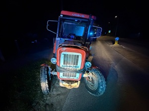pora nocna. Na drodze stoi stary, zniszczony czerwony ciągnik rolniczy Ursus. Przód ma owinięty kablem