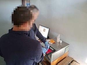 w pomieszczeniu technika kryminalistyki technik skanuje odciski palców zatrzymanego mężczyzny