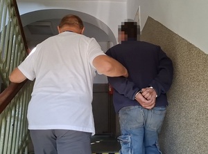 nieumundurowany policjant prowadzi schodami do góry mężczyznę, który ma ręce skute za plecami kajdankami