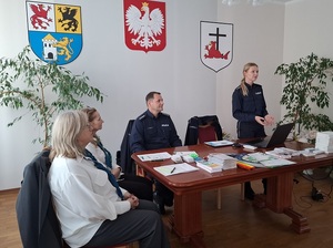 w sali urzędu miasta Łeby siedzą przy stole: policjant i dwie przedstawicielki ZUS. Obok stoi policjantka