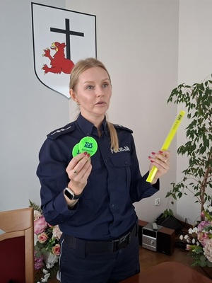 w sali stoi policjantka trzymająca w dłoniach elementy odblaskowe