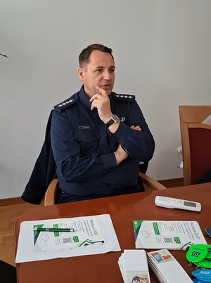 w sali przy stole siedzi policjant, który przemawia