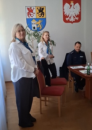w sali stoją dwie przedstawicielki ZUS. Jedna z nich przemawia. Obok przy stole siedzi policjant
