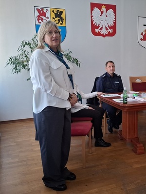 w sali stoi przemawiająca przedstawicielka ZUS. Obok przy stole siedzi policjant