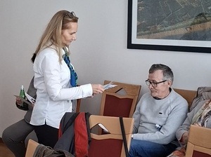 przedstawicielka ZUS rozdaje siedzącym na krzesłach seniorom ulotki