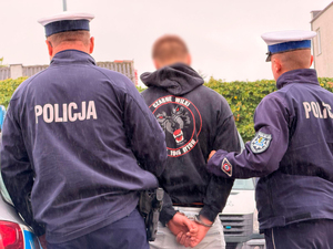 dwaj policjanci ruchu drogowego prowadzą mężczyznę, który ma ręce skute za plecami kajdankami